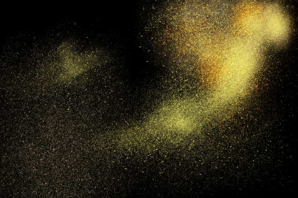 Freeze motion of yellow powder exploding, isolated on black, dark background. Abstract design of yellow dust cloud. Particles explosion screen saver, wallpaper.